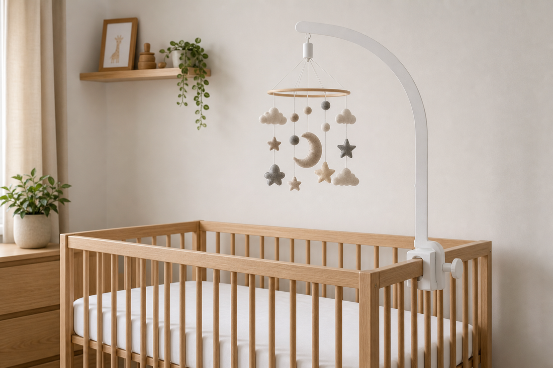 Straight-on view of a soft modern UK nursery with a white wooden cot mobile hanger secured to a light oak cot rail and a neutral felt mobile hanging high above a clear mattress with the wall left undecorated behind it