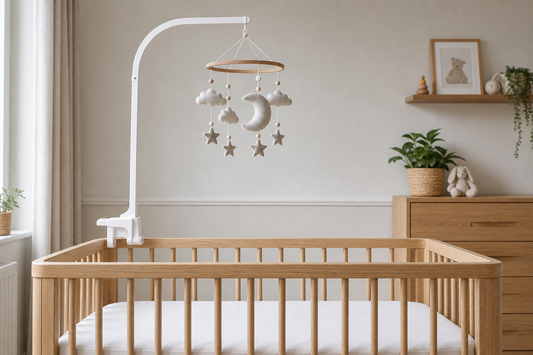 Straight-on cot-side view of a light oak cot with a securely fitted white wooden mobile hanger and a neutral moon-and-cloud felt mobile hanging high above a clear sleep space in a soft modern nursery