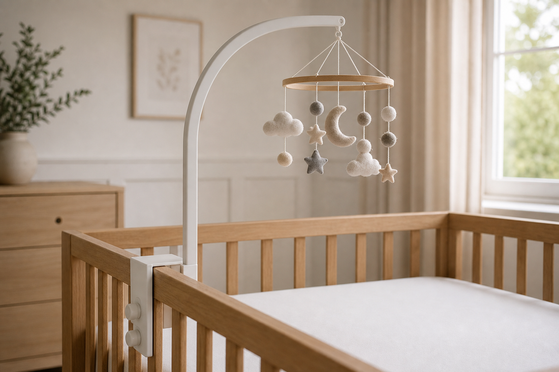 Detail-led view of a white wooden cot mobile hanger fixed securely to a light oak cot rail with a neutral felt mobile hanging high above a clear mattress in a soft modern UK nursery